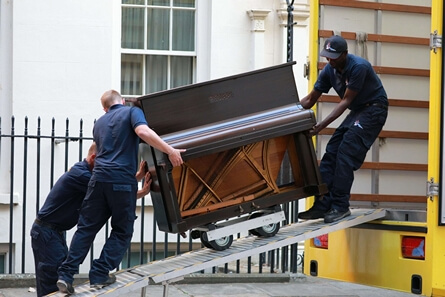 Three movers loading a piano into a yellow moving truck